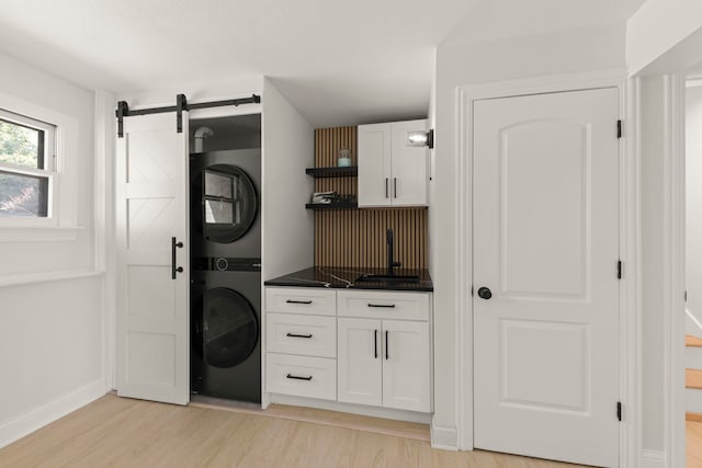 washroom with sink, light wood-type flooring, a barn door, and stacked washer / drying machine