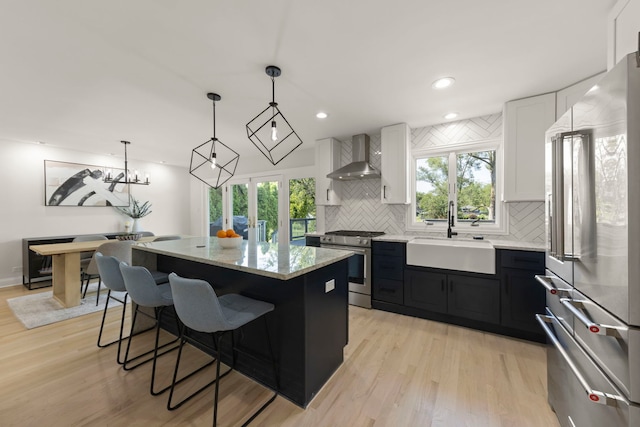 kitchen with pendant lighting, sink, white cabinets, wall chimney range hood, and appliances with stainless steel finishes