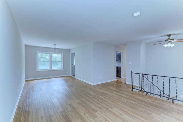 spare room with ceiling fan with notable chandelier and light hardwood / wood-style flooring