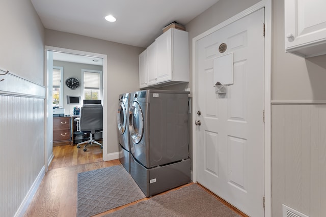 clothes washing area featuring light wood-type flooring, washing machine and dryer, and cabinets