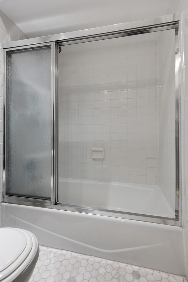 bathroom with enclosed tub / shower combo, tile patterned flooring, and toilet