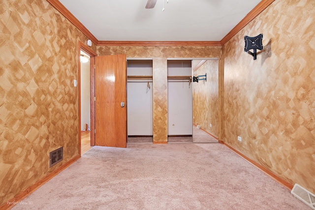 unfurnished bedroom featuring ornamental molding, light colored carpet, ceiling fan, and multiple closets