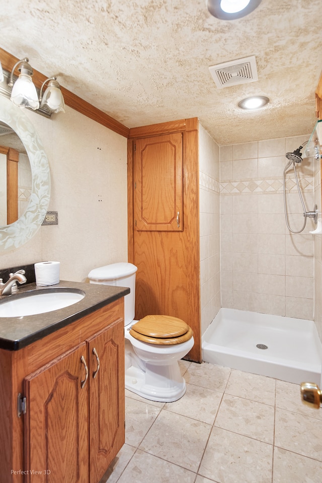 bathroom with tile patterned flooring, a textured ceiling, tiled shower, toilet, and vanity