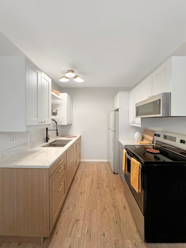 kitchen with light wood-type flooring, light stone counters, stainless steel appliances, sink, and white cabinets