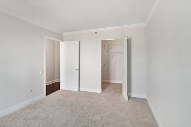 unfurnished bedroom featuring a spacious closet, ornamental molding, a closet, and light carpet