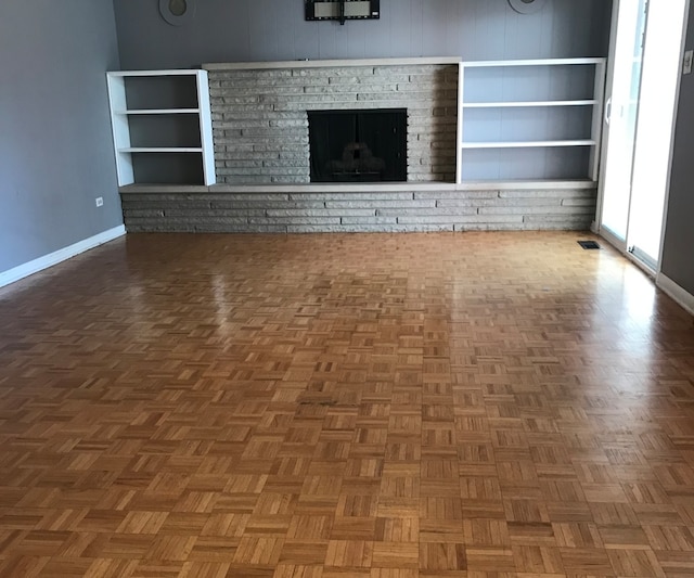 unfurnished living room featuring a brick fireplace and dark parquet floors