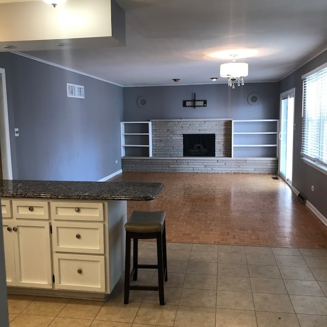 kitchen featuring crown molding, dark stone countertops, and a fireplace