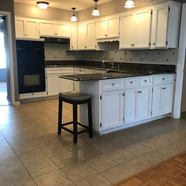 kitchen with white cabinets, hanging light fixtures, double oven, a breakfast bar, and dark stone countertops