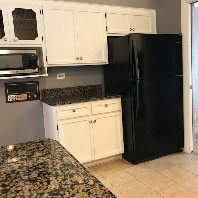 kitchen with stainless steel microwave, dark stone countertops, black fridge, and white cabinets