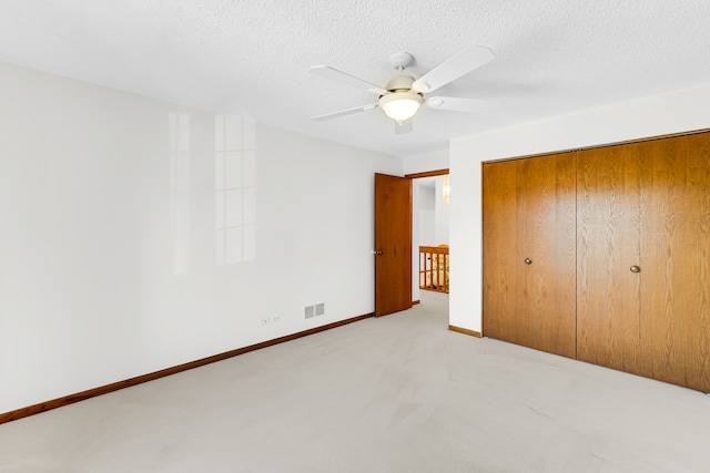 unfurnished bedroom featuring a closet, light colored carpet, ceiling fan, and a textured ceiling