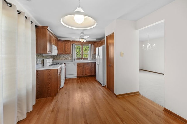 kitchen with pendant lighting, white appliances, light hardwood / wood-style flooring, backsplash, and ceiling fan with notable chandelier