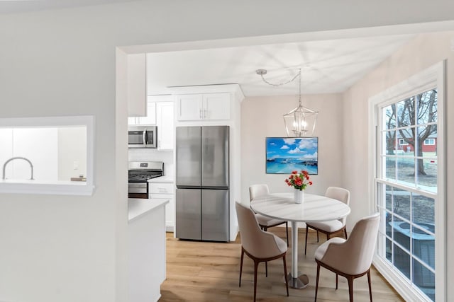 kitchen with appliances with stainless steel finishes, white cabinetry, an inviting chandelier, light hardwood / wood-style floors, and decorative light fixtures