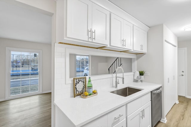 kitchen featuring white cabinetry, sink, decorative backsplash, stainless steel dishwasher, and light hardwood / wood-style flooring