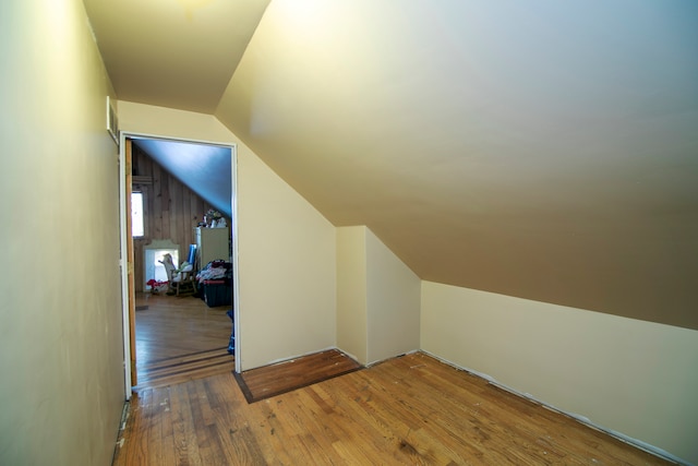 additional living space with wood walls, vaulted ceiling, and hardwood / wood-style flooring