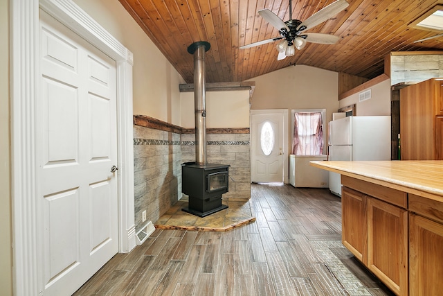 kitchen with white refrigerator, wood-type flooring, wood ceiling, vaulted ceiling, and a wood stove