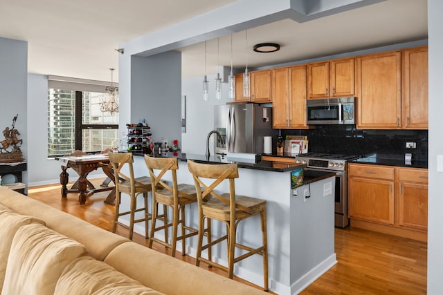 kitchen featuring appliances with stainless steel finishes, a breakfast bar area, an island with sink, and decorative light fixtures