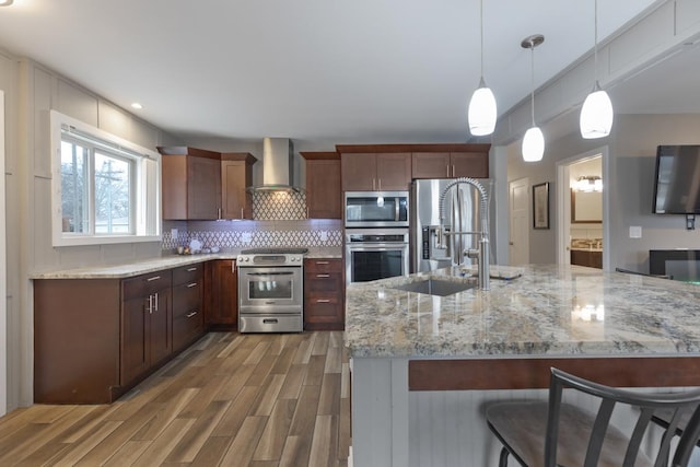 kitchen featuring backsplash, wall chimney exhaust hood, stainless steel appliances, a sink, and wood finished floors