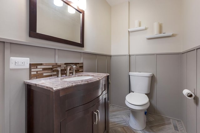 bathroom featuring a decorative wall, tasteful backsplash, vanity, a wainscoted wall, and toilet