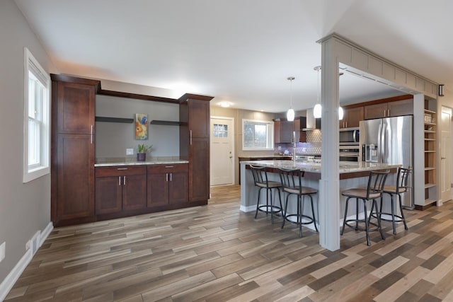 kitchen with tasteful backsplash, open shelves, appliances with stainless steel finishes, light wood-style flooring, and a breakfast bar area