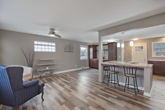 kitchen with wood-type flooring, a breakfast bar area, a center island with sink, decorative light fixtures, and ceiling fan