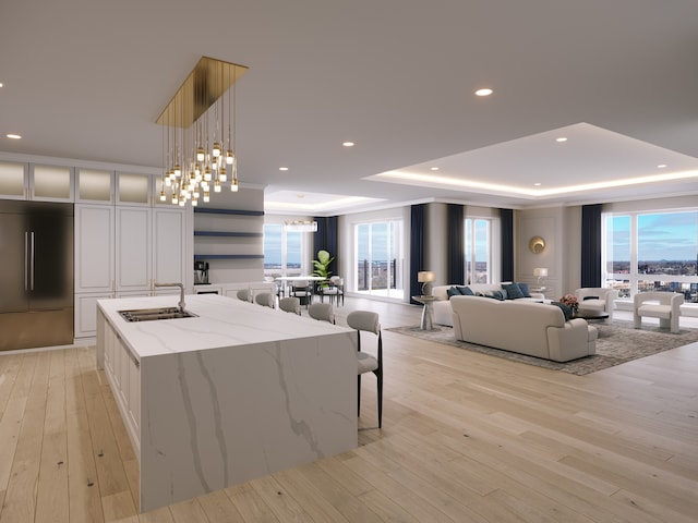 kitchen with a large island with sink, white cabinetry, light stone counters, built in fridge, and a tray ceiling