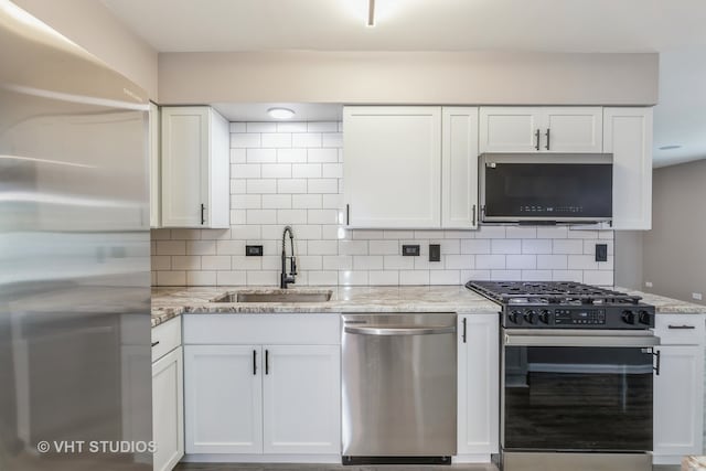 kitchen with light stone counters, tasteful backsplash, white cabinets, stainless steel appliances, and sink