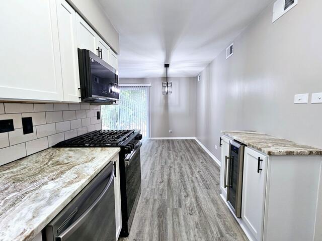 kitchen featuring appliances with stainless steel finishes, light hardwood / wood-style floors, white cabinetry, and light stone counters