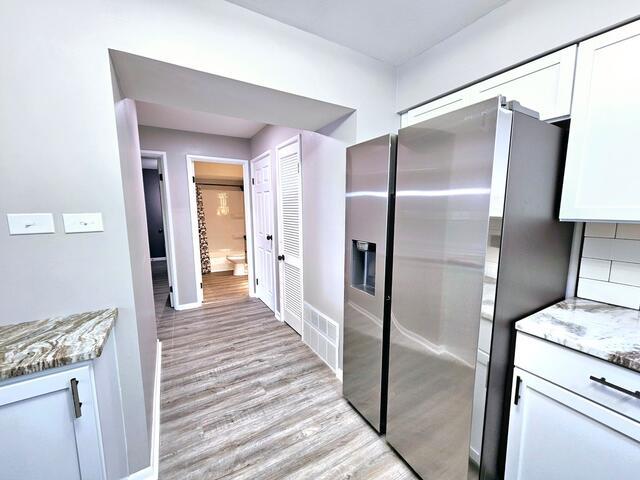 kitchen featuring stainless steel refrigerator with ice dispenser, light hardwood / wood-style floors, white cabinetry, and dark stone countertops