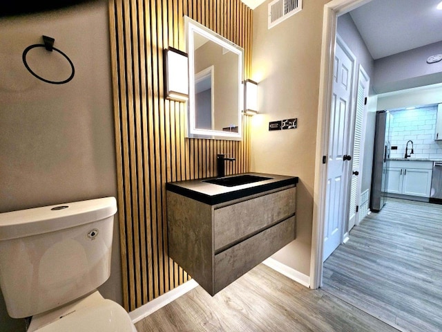 bathroom featuring wood-type flooring, backsplash, vanity, and toilet