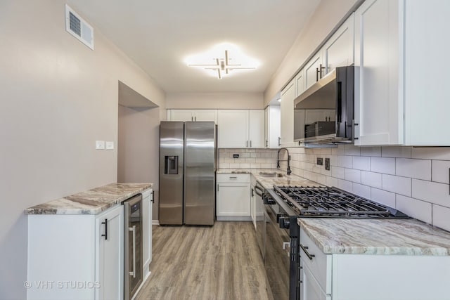 kitchen with light wood-type flooring, sink, white cabinets, stainless steel appliances, and backsplash