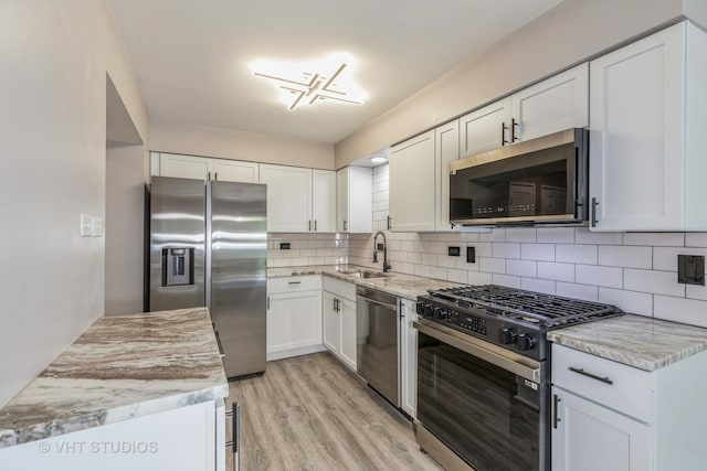 kitchen with appliances with stainless steel finishes, light hardwood / wood-style floors, white cabinets, backsplash, and sink