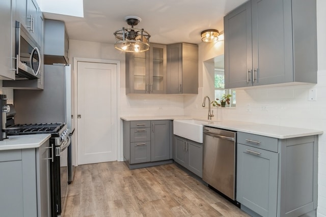 kitchen featuring appliances with stainless steel finishes, gray cabinetry, backsplash, light wood-type flooring, and sink