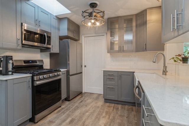 kitchen featuring gray cabinetry, decorative light fixtures, stainless steel appliances, light hardwood / wood-style floors, and decorative backsplash