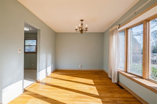 unfurnished room featuring an inviting chandelier and light hardwood / wood-style flooring