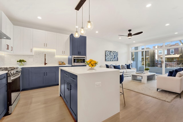 kitchen featuring white cabinetry, stainless steel gas range oven, sink, and decorative light fixtures