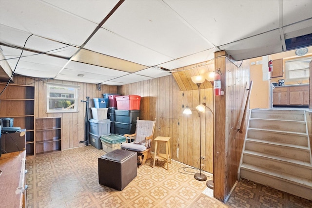 below grade area with wood walls, tile patterned floors, a paneled ceiling, and stairs