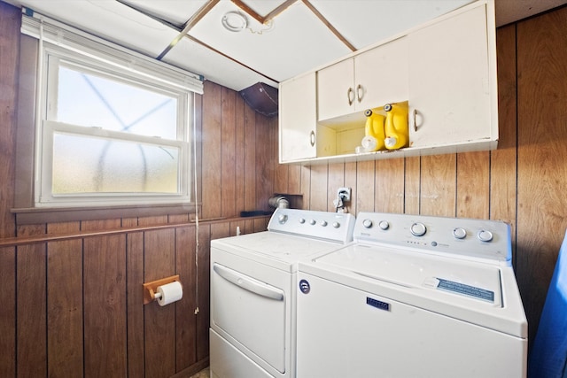 laundry area with wooden walls, separate washer and dryer, and cabinets