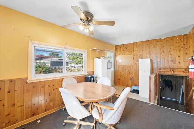 carpeted dining space with ceiling fan and wood walls