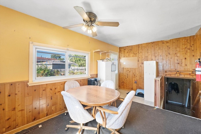 dining space featuring wooden walls, wainscoting, and a ceiling fan