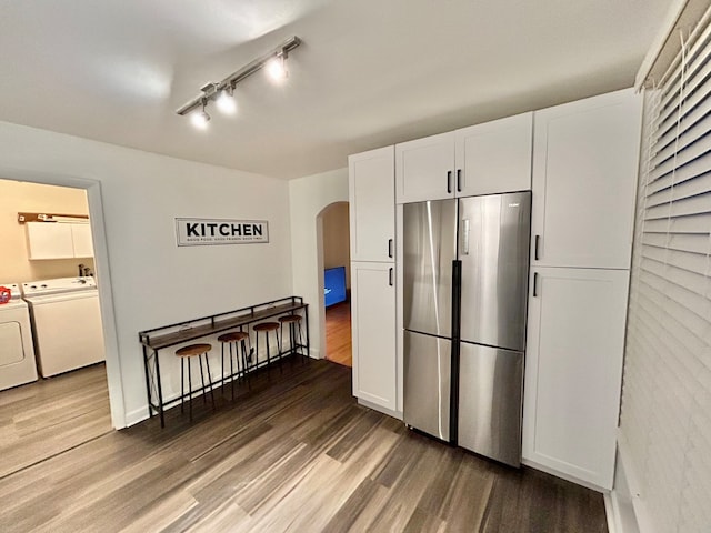 kitchen featuring track lighting, hardwood / wood-style flooring, white cabinets, stainless steel refrigerator, and independent washer and dryer