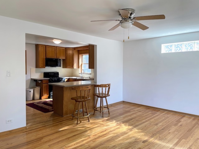 kitchen featuring light wood-type flooring, black appliances, kitchen peninsula, and a healthy amount of sunlight