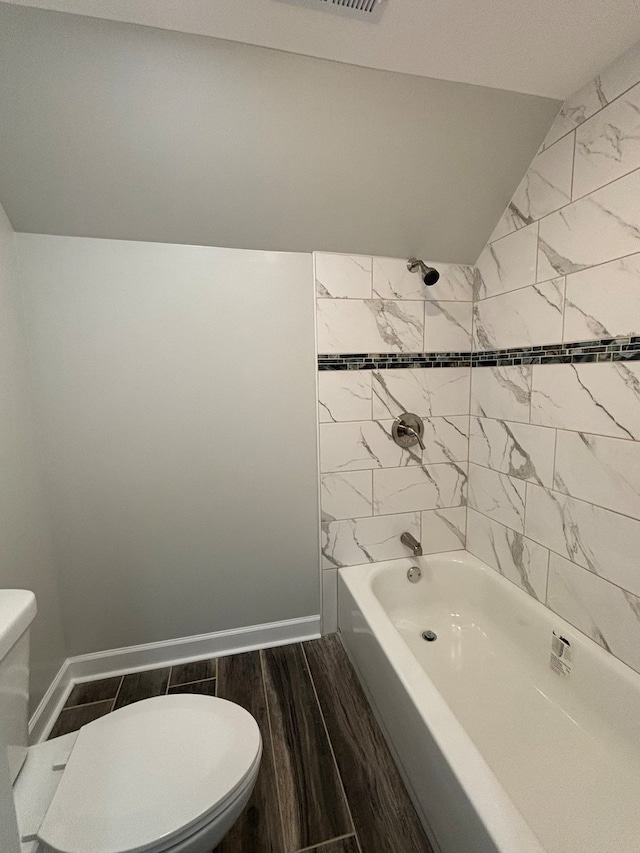 bathroom with hardwood / wood-style floors, lofted ceiling, toilet, and tiled shower / bath