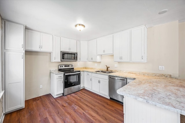 kitchen with appliances with stainless steel finishes, white cabinets, kitchen peninsula, dark hardwood / wood-style flooring, and sink