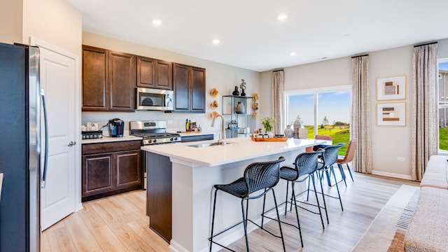 kitchen with a kitchen breakfast bar, stainless steel appliances, sink, a center island with sink, and light hardwood / wood-style floors