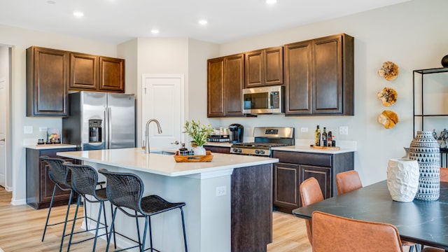 kitchen with sink, an island with sink, a kitchen bar, appliances with stainless steel finishes, and light wood-type flooring