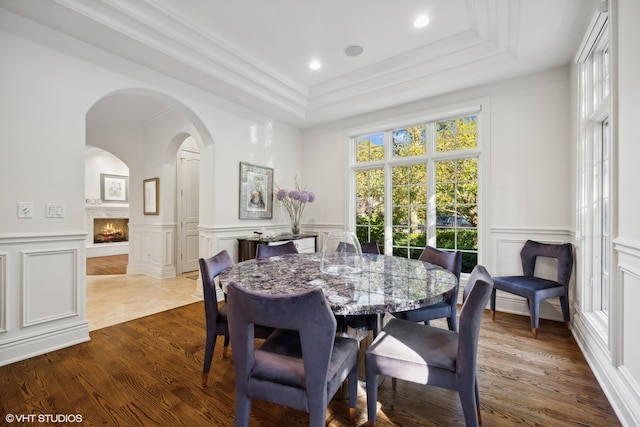 dining area featuring a fireplace, wood-type flooring, a raised ceiling, and ornamental molding