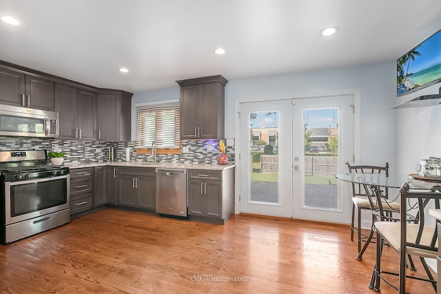 kitchen featuring appliances with stainless steel finishes, a healthy amount of sunlight, light wood-type flooring, and tasteful backsplash