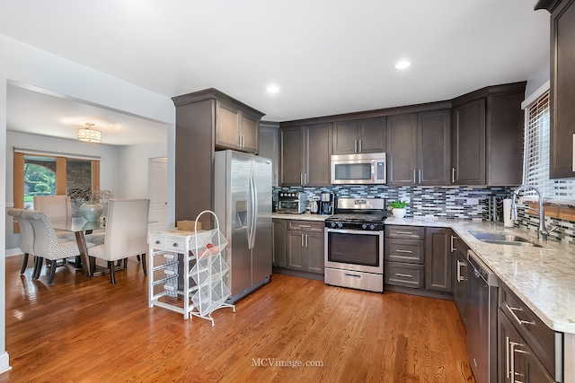 kitchen featuring light wood-type flooring, light stone counters, sink, backsplash, and appliances with stainless steel finishes