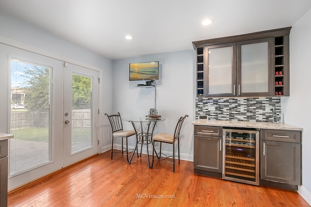 bar with light hardwood / wood-style flooring, beverage cooler, light stone counters, and decorative backsplash