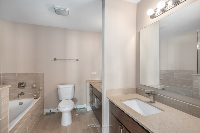 bathroom featuring tiled tub, vanity, and toilet